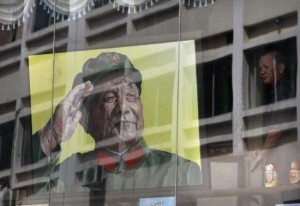 A man looks out from a window next to a portrait of late Chinese leader Deng in a gallery at Dafen Oil Painting Village, in Shenzhen