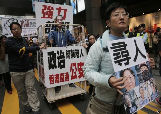 A protester wearing a mask of bookseller Lee Bo stands in a cage during a protest against the disappearances of booksellers in Hong Kong