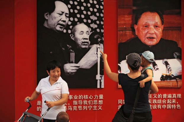 A mother (C) shows her child pictures of former communist party leaders Mao Zedong (top L) and Deng Xiaoping (top R) in Ditan Park in Beijing