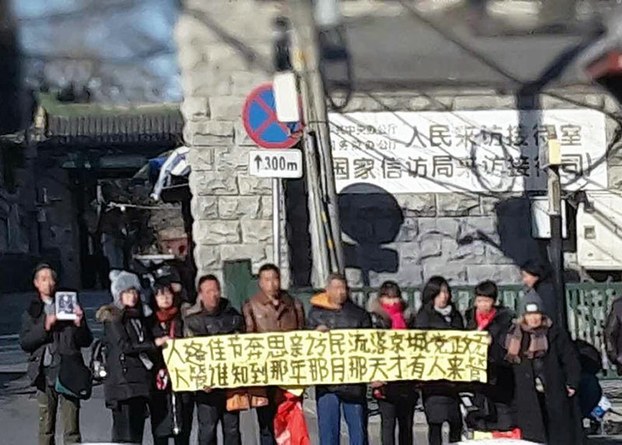 Petitioners in Beijing (faces obscured) hold a banner demanding government intervention in their cases