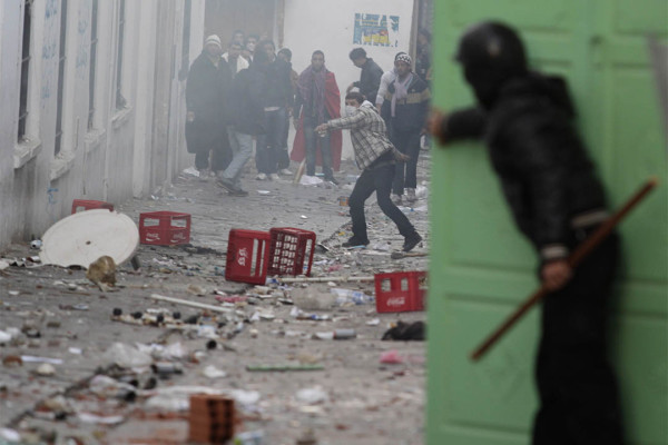 A Tunisian riot policeman takes shelter behind a door while protesters throw stones during clashes in Tunis January 28, 2011. Tunisian riot police on Friday destroyed the makeshift camp set up by anti-government protesters outside the prime minister's office, while Islamists marched through central Tunis demanding religious freedom. REUTERS/Zohra Bensemra (TUNISIA - Tags: POLITICS CIVIL UNREST IMAGES OF THE DAY) - RTXX7L2