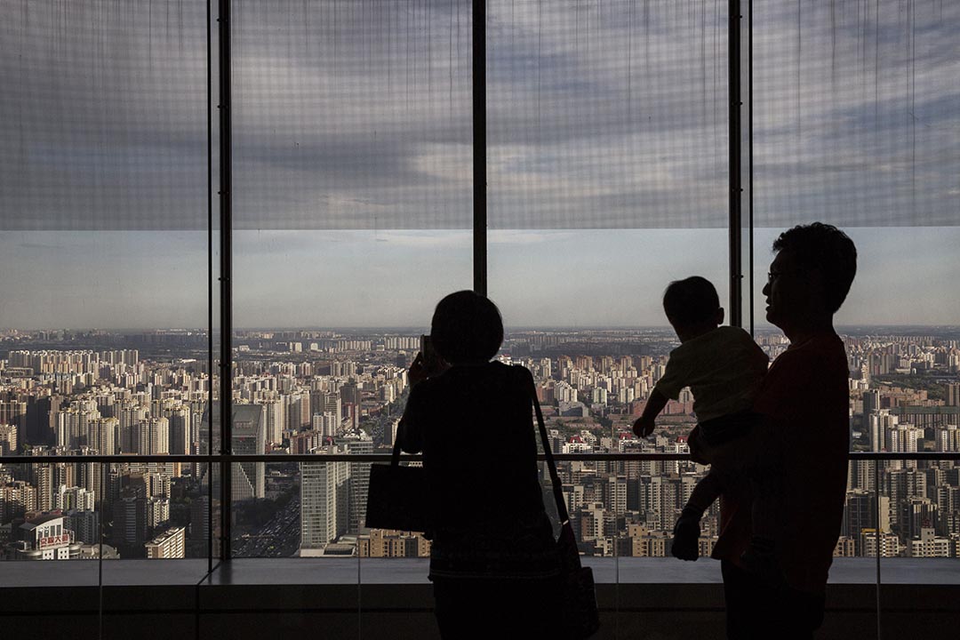 BEIJING, CHINA - JUNE 11:  A Chinese couple hold stand with their child as they look out on residential and office buildings from a luxury hotel on June 11, 2015 in Beijing, China. The area is the financial centre of China's capital city. (Photo by Kevin Frayer/Getty Images)